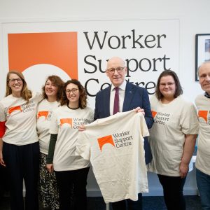 John Swinney MSP holds WSC t-shirt, surrounded by WSC team in WSC t-shirts in WSC office.